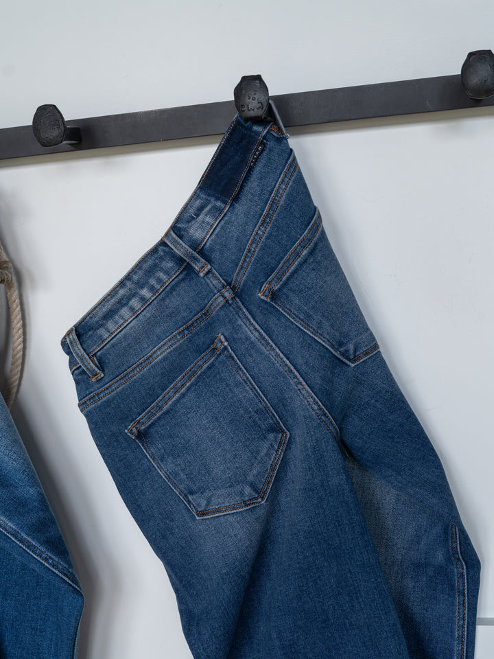 The Britton High Rise Wide Leg Crop Jean by Savannah Sevens western life{&}style hangs by a belt loop on a black wall hook against a white background.