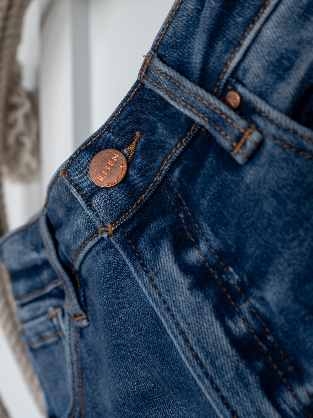 Close-up of The Britton High Rise Wide Leg Crop Jean in blue denim by Savannah Sevens western life{&}style, featuring a copper button with engraved branding, visible stitching, and part of a belt loop—ideal for fans of high rise, wide leg crop jeans.