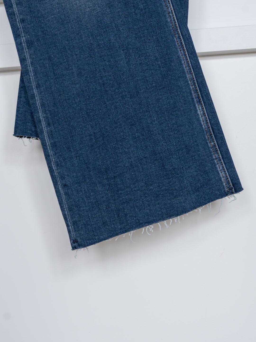 A close-up of the raw, frayed bottom hems of The Britton High Rise Wide Leg Crop Jean by Savannah Sevens western life{&}style in blue, hanging against a plain white background.