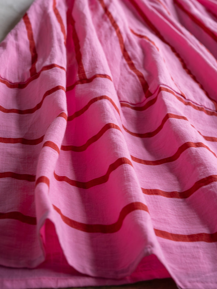 A close-up of The Fredonia dress by Savannah Sevens western life{&}style shows pink and red wavy horizontal stripes, creating a soft, flowing texture with gentle folds.