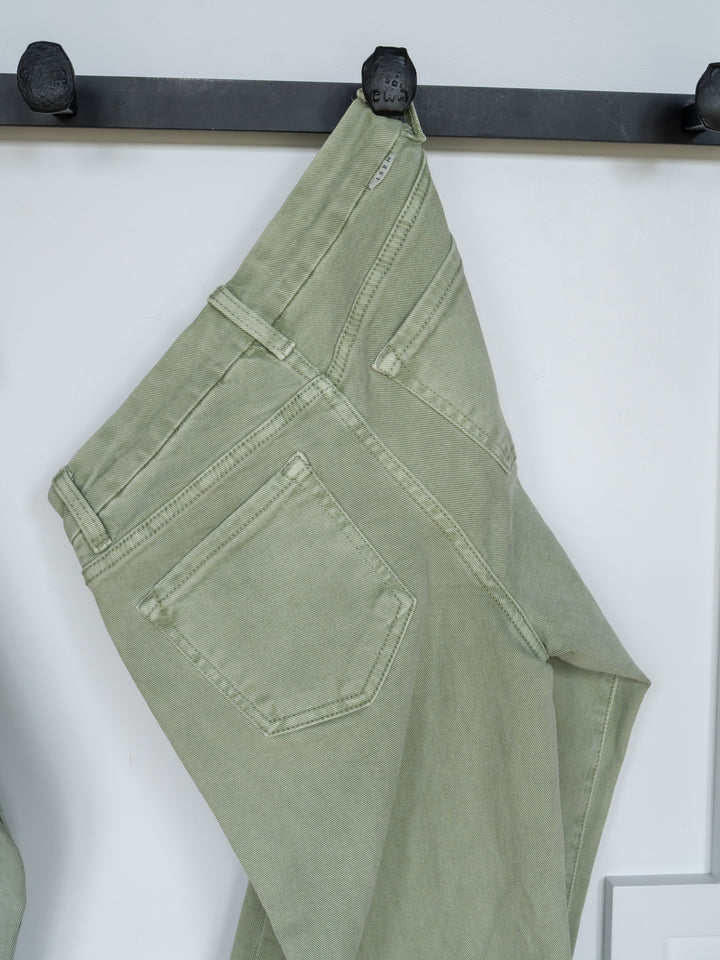 The Lindy High Rise Wide Leg Jean by Savannah Sevens western life{&}style hangs by a belt loop on a black hook against a white background, displaying the sage denim’s back pockets, seams, and raw cut hem.