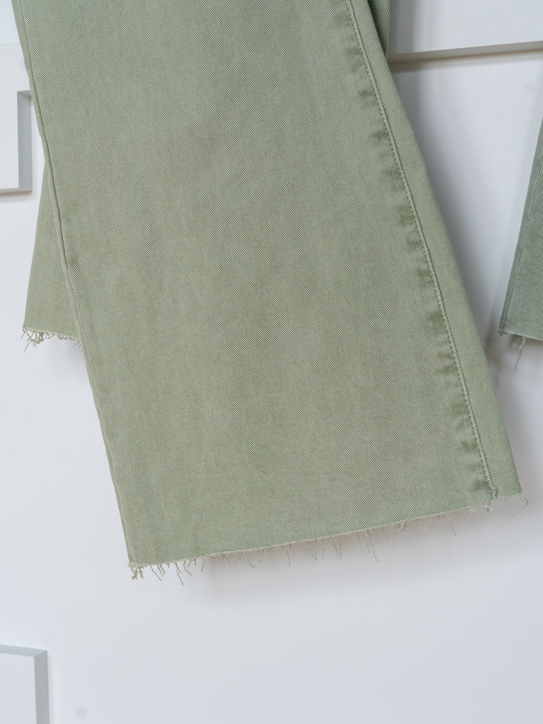 Close-up of The Lindy High Rise Wide Leg Jean by Savannah Sevens western life{&}style, featuring sage denim pant legs with a raw cut hem, hanging against a white background.