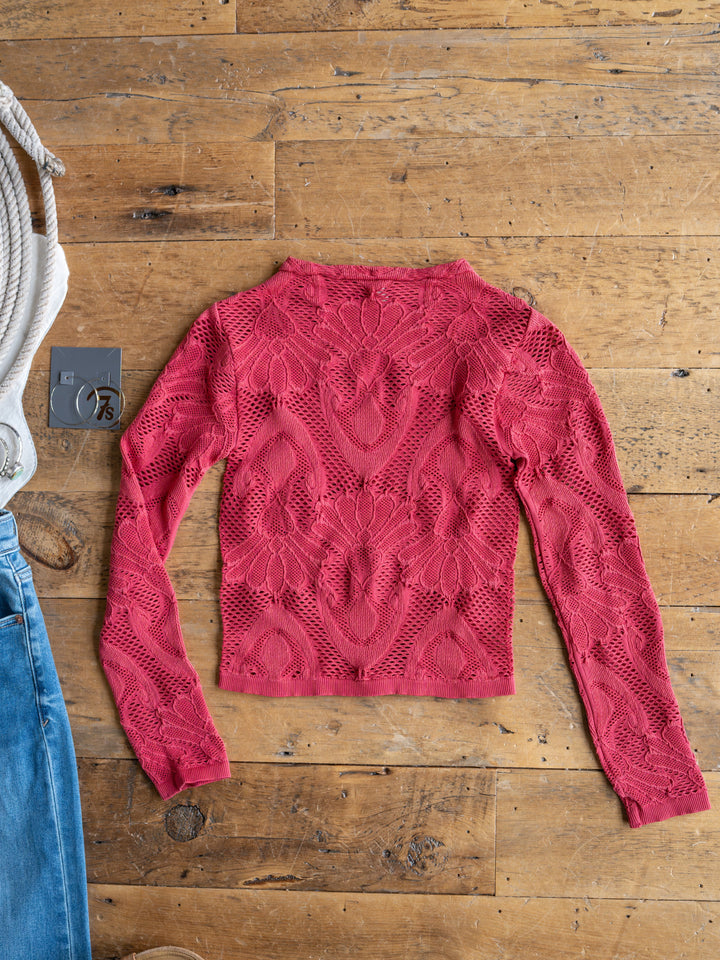 The Lexa by Savannah Sevens western life{&}style, a bright pink long sleeve sheer crochet floral top, is laid flat on a wooden floor beside blue jeans, a gray tag, and a white coiled rope.