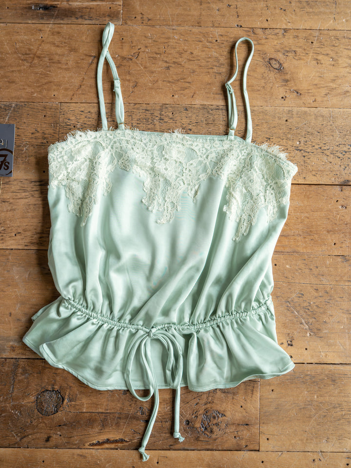 The Swansea by Savannah Sevens western life{&}style: light green satin sleeveless top with lace chest overlay, adjustable straps, and drawstring waist, laid flat on a wooden surface.