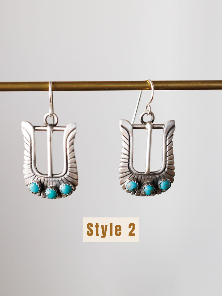 The Los Alamos Earrings by Savannah Sevens western life{&}style are sterling silver buckle-shaped earrings with three turquoise stones at the base, suspended from a horizontal rod. “Style 2” is shown below these unique turquoise earrings.