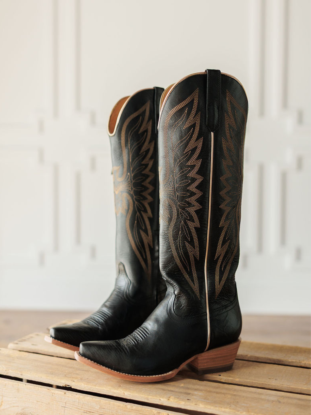 The Vaquera by Savannah Sevens western life{&}style—black leather snip toe boots with brown western embroidery—rest atop a wooden crate, set against a light, decorative backdrop. Made by Black Star. 