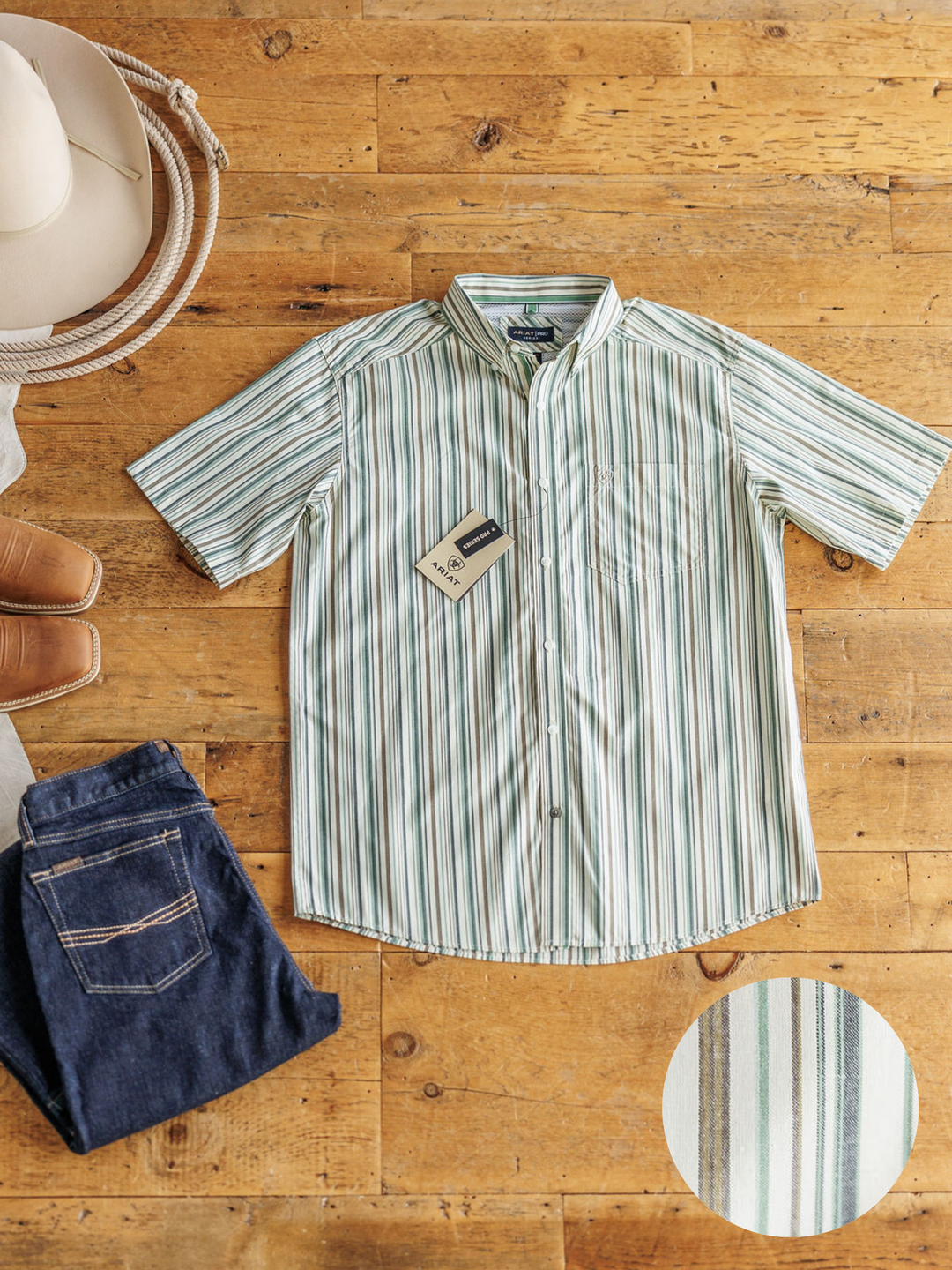The Austwell men's shirt by Savannah Sevens western life&style, in light green and white stripes, is laid flat on a wooden floor with blue jeans, tan boots, and a cowboy hat. Inset: close-up of the short sleeve button-up's fabric pattern.