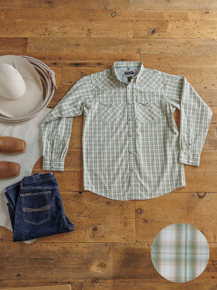 The Eastwood men's plaid snap shirt by Savannah Sevens western life&style is displayed on a wooden floor with blue jeans, brown boots, a white cowboy hat, and a coiled rope; a circular inset shows the fabric pattern.