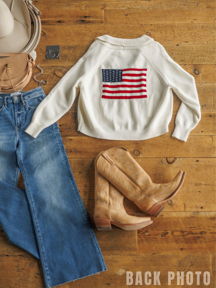 Flat lay of The American Classic {Exclusive} cardigan by Savannah Sevens western life{&}style, blue jeans, tan cowboy boots, a tan hat, and a tan purse on a wooden floor. "BACK PHOTO" appears in the lower right corner.
