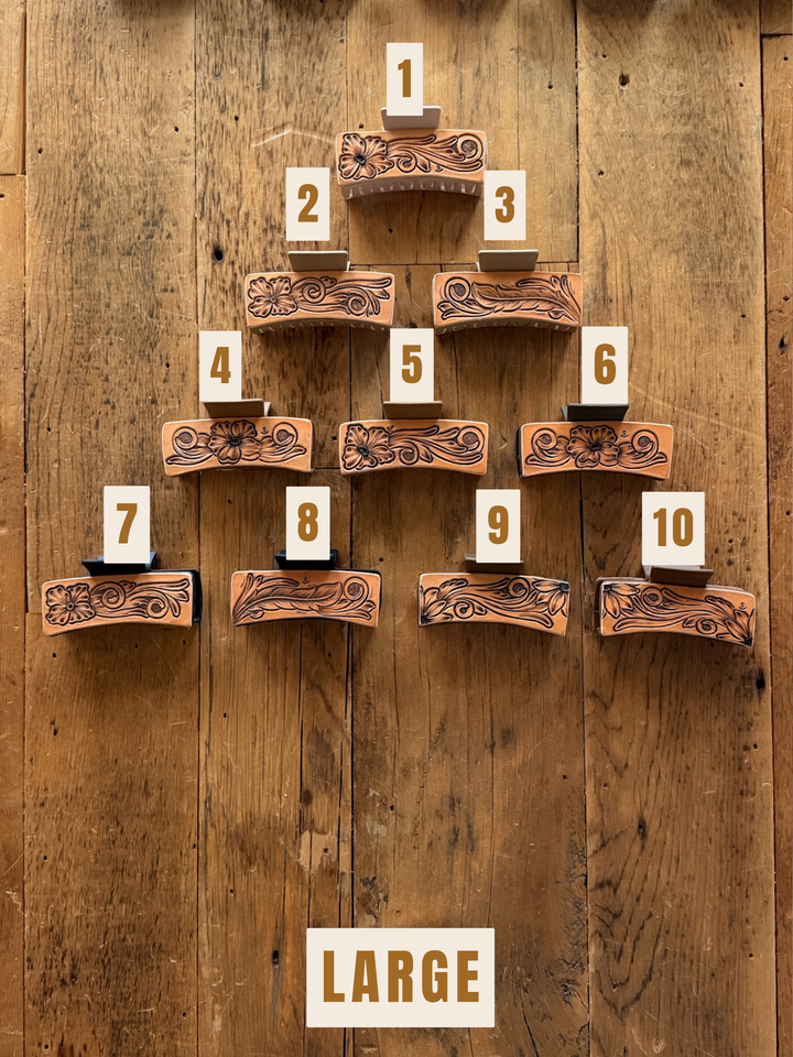 Ten unique hand-tooled leather Campitos Claw Clips from Savannah Sevens western life&style arranged in a pyramid on a wooden surface, each labeled with a number from 1 to 10.