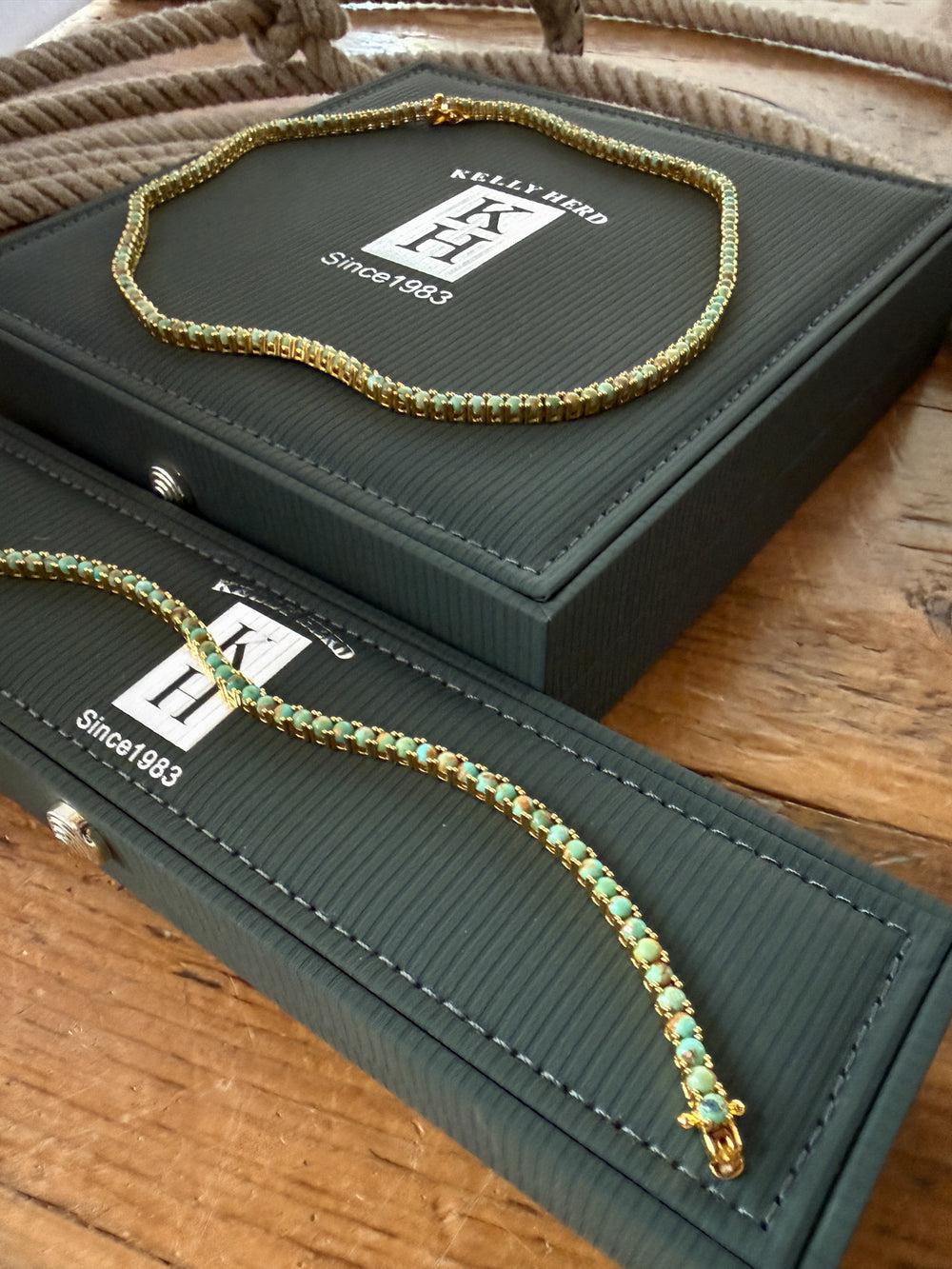 A Kingman Turquoise Gold Tennis Necklace by Savannah Sevens western life{&}style is displayed on dark green Kelly Herd jewelry boxes atop a wooden surface.
