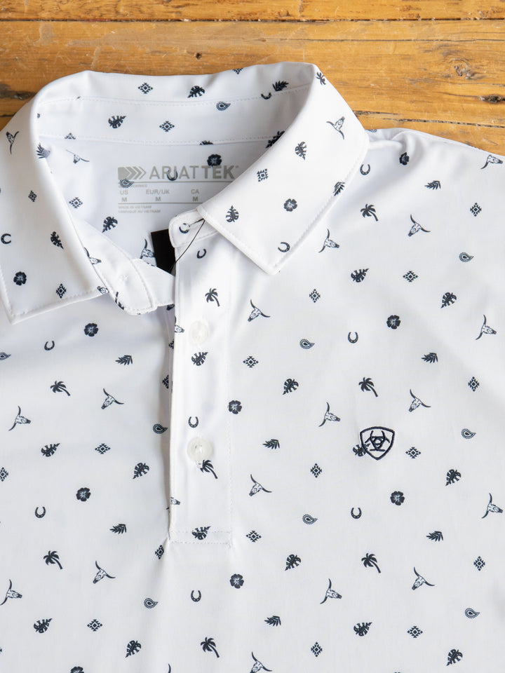The Prescott Ariat Men's Western Graphic Polo by Savannah Sevens western life{&}style is a white shirt with black palm trees, horseshoes, and tropical drinks. It offers moisture-wicking comfort and is neatly displayed on a wooden surface.