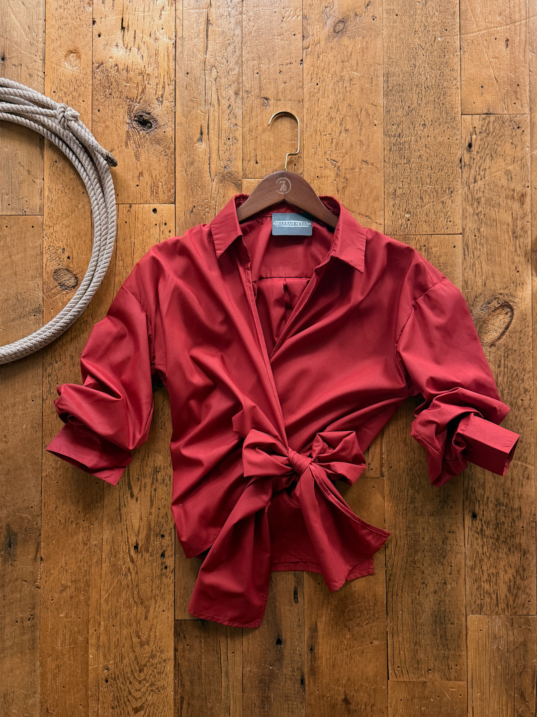 Altamont Red Wrap Top, a red cotton blend 3/4 sleeve wrap top with a front tie, hanging on a wooden hanger against a wooden surface.