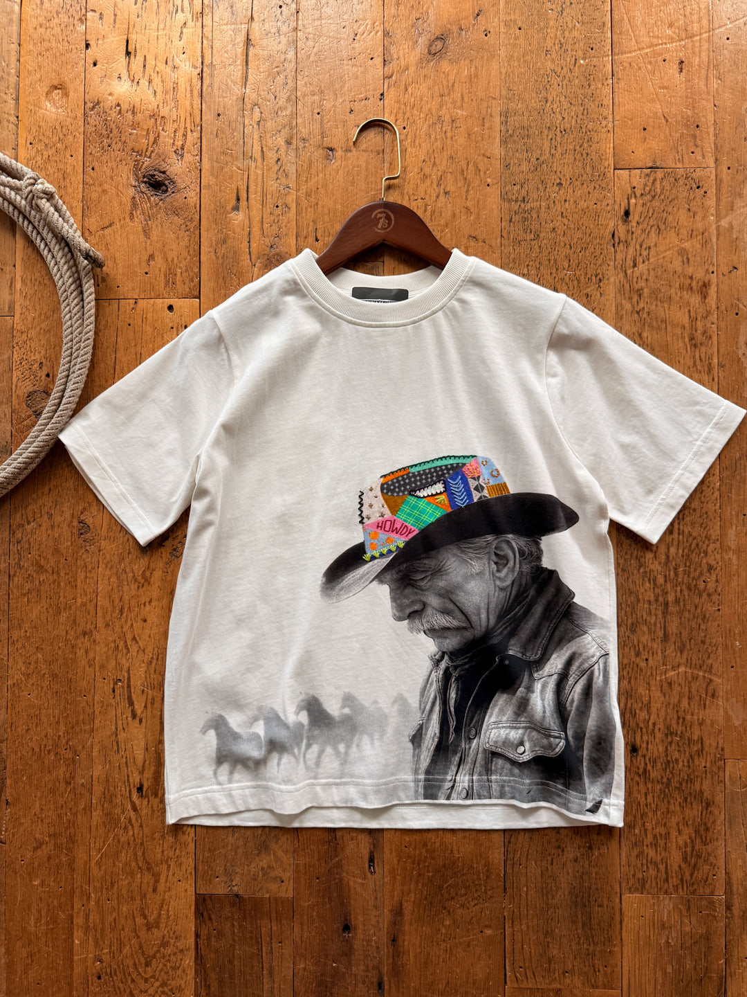 Off-white, heavyweight cotton Reverie Cowboy Graphic Tee featuring a black-and-white print of a cowboy in a colorful, patterned hat and a herd of running horses.