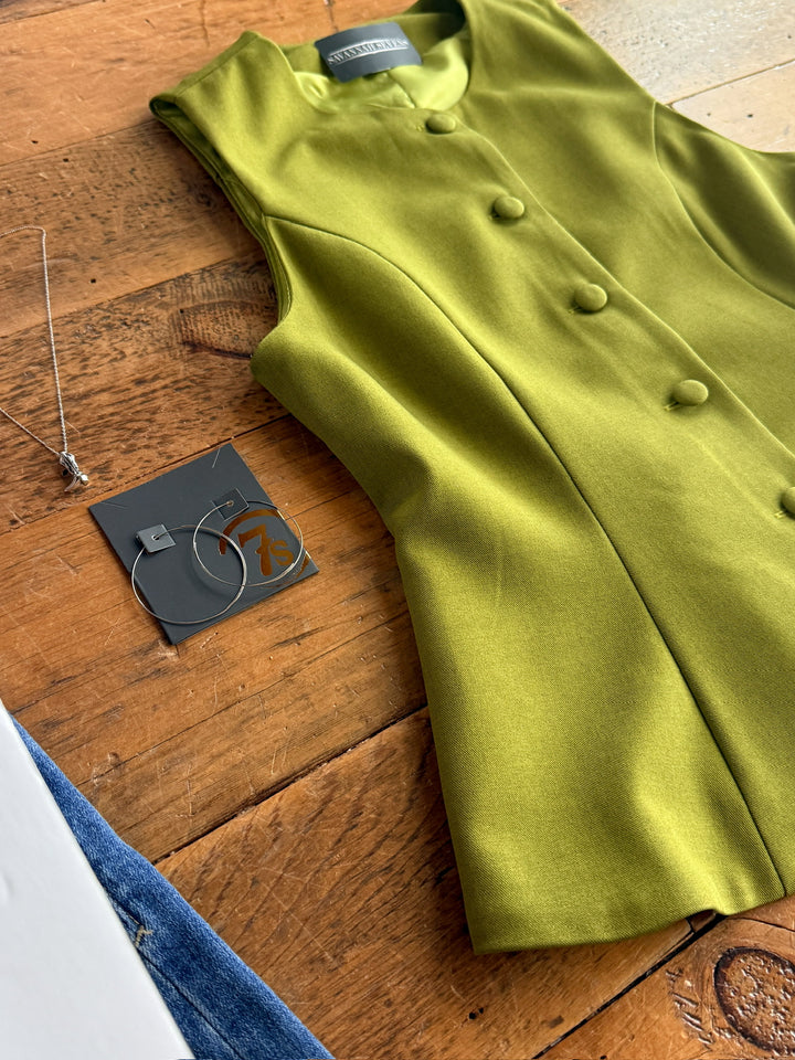 The Pamona by Savannah Sevens western life{&}style, an olive sleeveless button-up top with a tailored fit, is displayed on a wooden surface next to a silver necklace, hoop earrings on a card, and blue jeans at the edge.