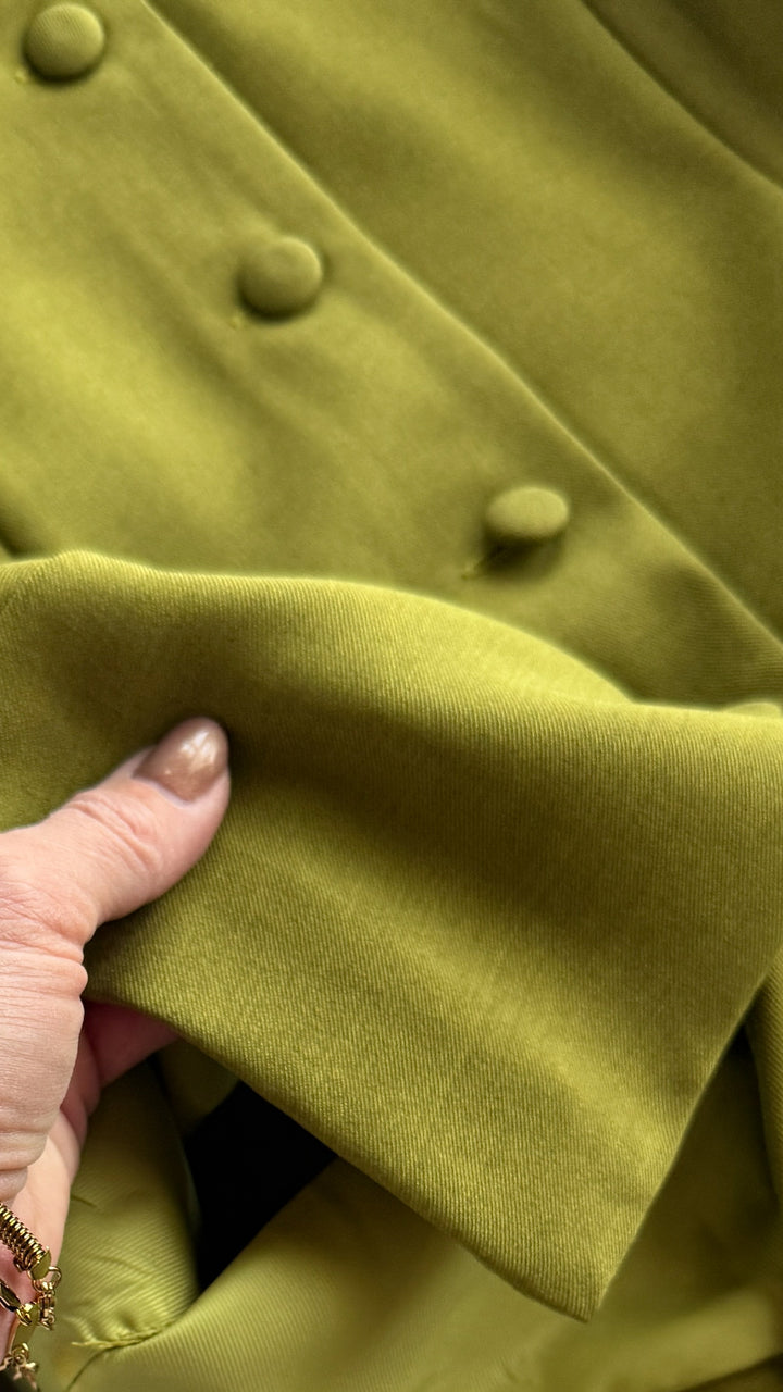 A hand holds The Pamona, an olive sleeveless top by Savannah Sevens western life{&}style, featuring fabric-covered buttons for a tailored look.