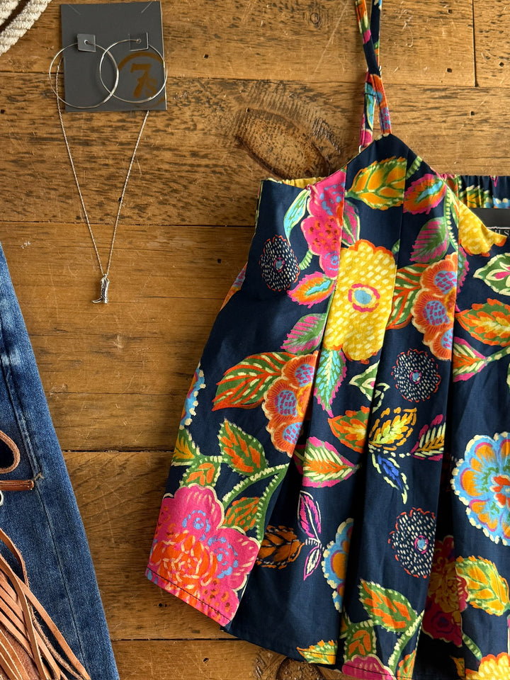 The Pacifica by Savannah Sevens western life{&}style is a vibrant cotton floral sleeveless top displayed on wood, paired with hoop earrings, a silver necklace, and partially visible blue fringe jeans.