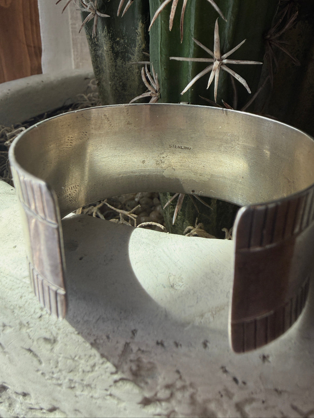 The Vallejo Cuff by Savannah Sevens western life{&}style sits on a textured white pot with a green cactus behind it. Sunlight highlights the vintage turquoise details on this elegant sterling silver bracelet.