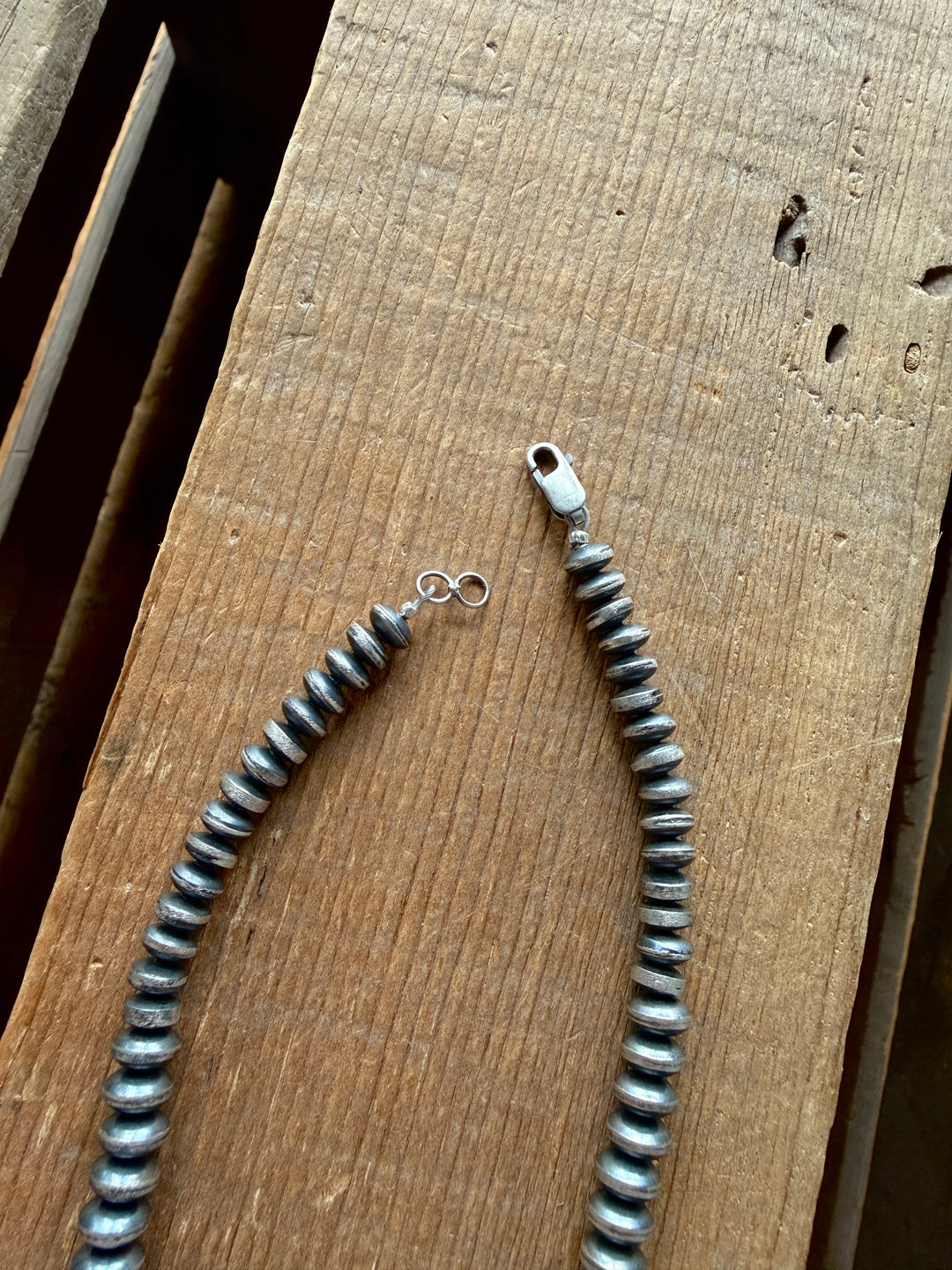 A close-up of the 20.5-inch Saledo Necklace by Savannah Sevens western life{&}style, featuring graduated sterling silver Navajo pearl rondelle beads and a metal clasp, displayed on a textured wooden surface with the open clasp showing both ends.