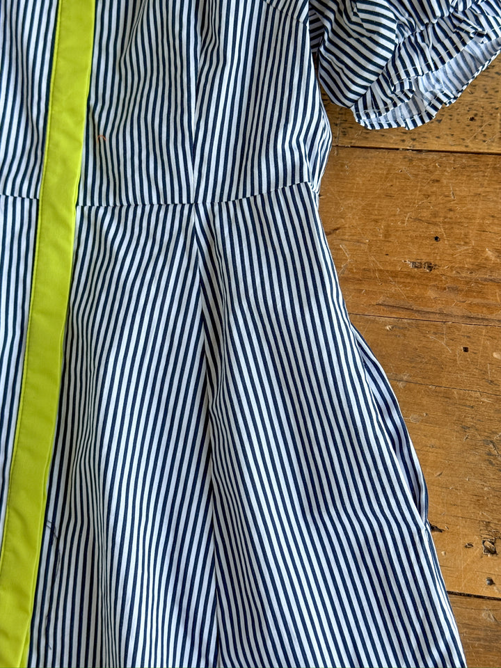 A close-up of The Tererro by Savannah Sevens western life{&}style, a blue and white pinstripe cotton midi dress with a yellow stripe, puff sleeve detail, and gathered waist, laid on a wooden surface.