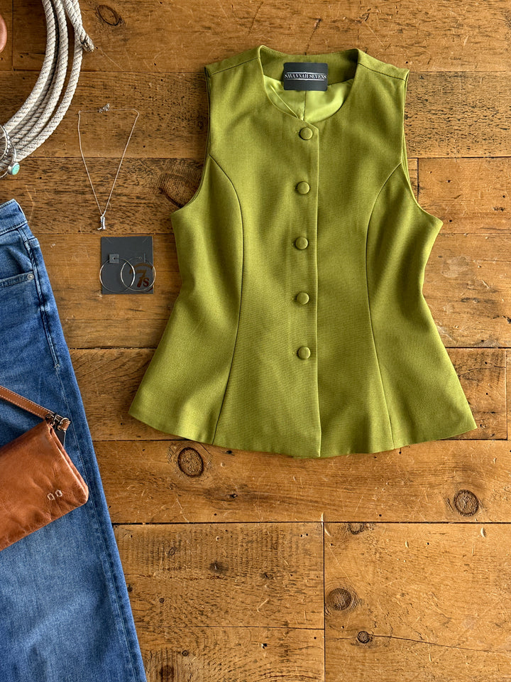 The Pamona by Savannah Sevens western life{&}style, an olive sleeveless top with buttons, is displayed flat next to blue jeans, a brown leather purse, a silver necklace, and a coiled rope on a wooden surface.