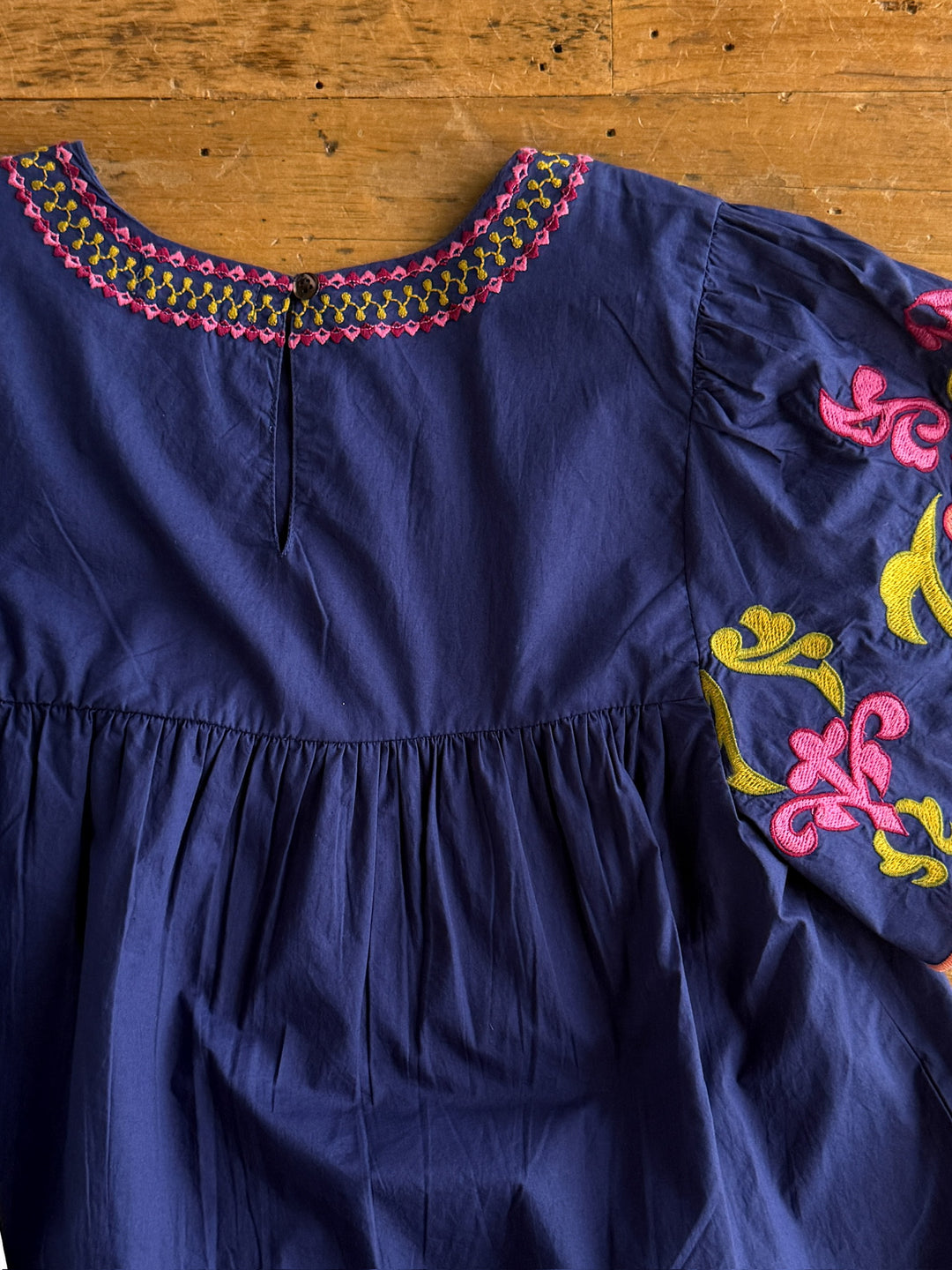 The Montevello by Savannah Sevens western life{&}style is a navy cotton flutter sleeve blouse with pink and yellow floral embroidery on the neckline and sleeves, featuring detailed embroidered patterns for a stylish touch.