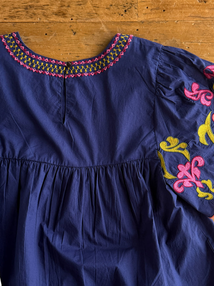 The Montevello by Savannah Sevens western life{&}style is a navy cotton flutter sleeve blouse with pink and yellow floral embroidery on the neckline and sleeves, featuring detailed embroidered patterns for a stylish touch.
