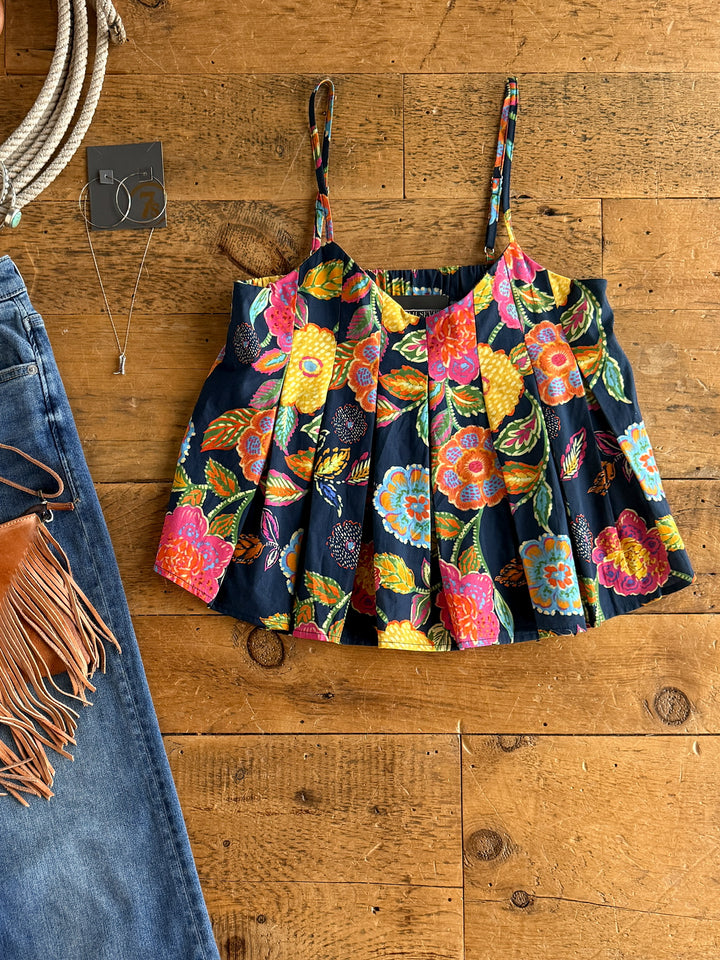 The Pacifica floral crop top by Savannah Sevens western life{&}style, featuring spaghetti straps, is displayed on wood next to blue jeans with brown fringe, a pendant necklace, and a partially visible coiled rope.