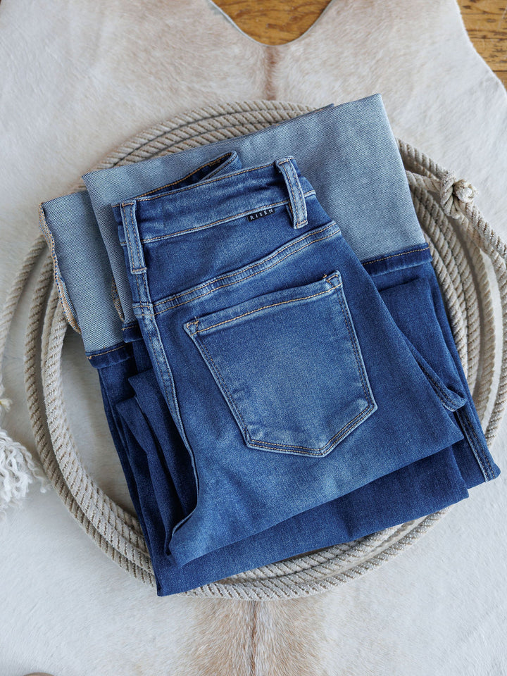 Two pairs of blue jeans, including The Maren High Rise Wide Leg Jean by Savannah Sevens western life{&}style, are folded and stacked on a coiled rope atop a light-colored animal hide rug.