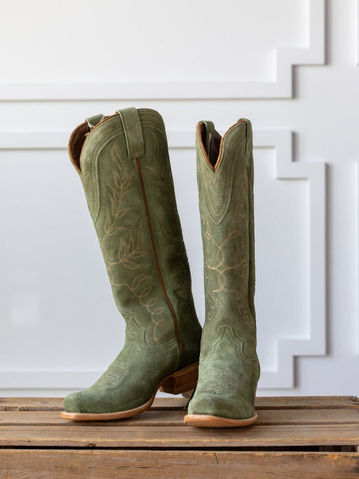 A pair of tall, green The Hyer Abbyville Boot by Savannah Sevens western life{&}style with decorative stitching and square toes stands side by side on a wooden surface against a white paneled background.