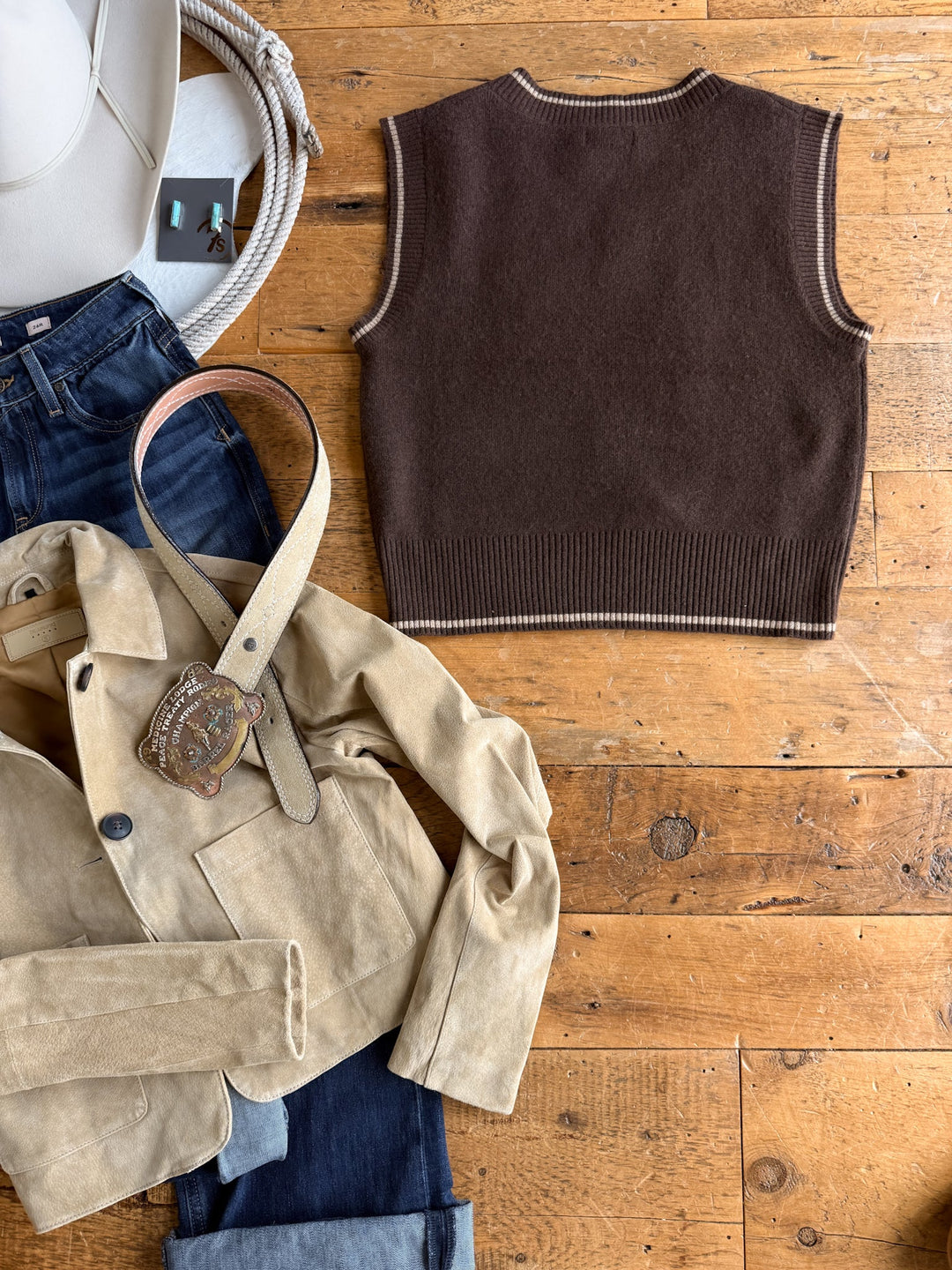 Outfit laid on wood floor: jeans, beige suede jacket with a belt and large buckle, Savannah Sevens western life{&}style Abilene Boot Stitch Sweater Vest in chocolate, white hat, and coiled rope in the corner.