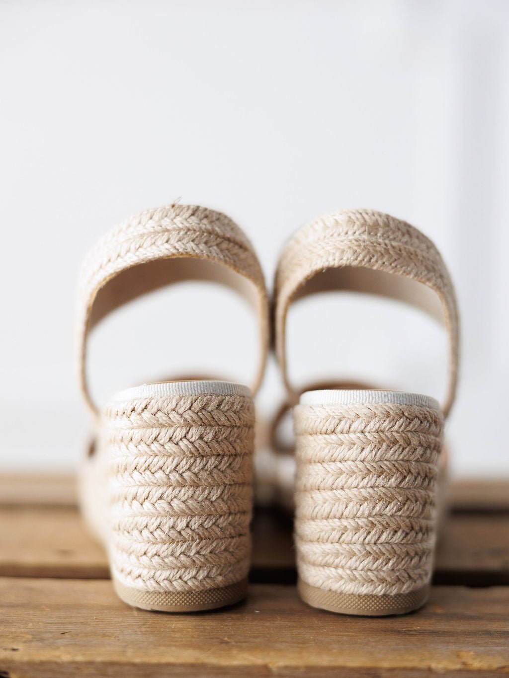 A close-up of The Abilene by Savannah Sevens western life{&}style—open toe beige woven wedge sandals with a gold snaffle bit and thick heels, displayed on wood with a white background.