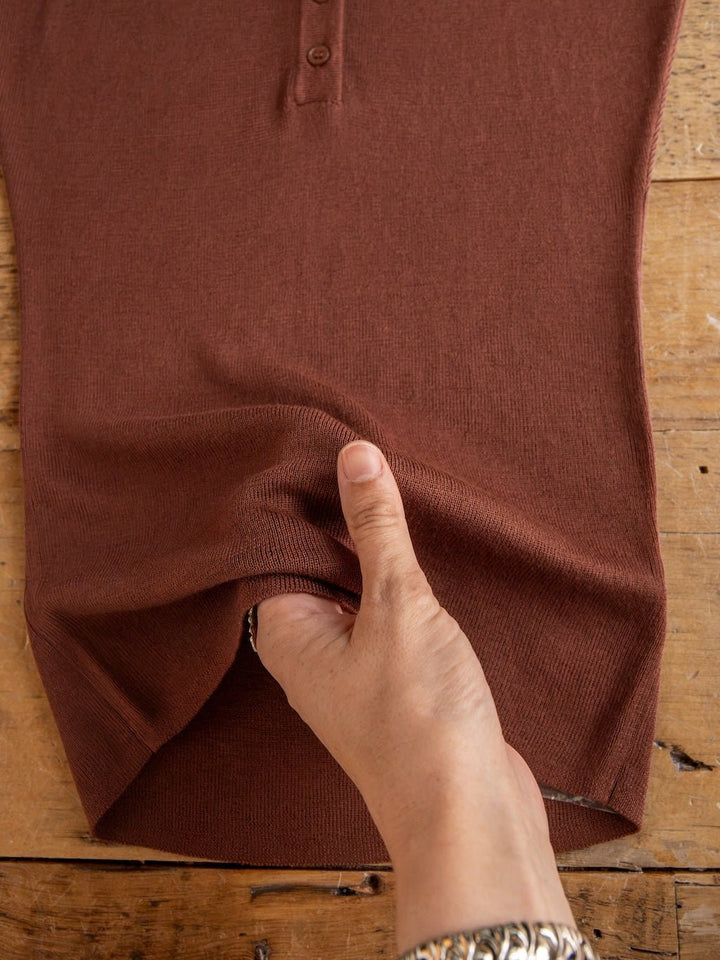 A hand stretches the fabric of the Adair Chestnut Cap Sleeve Top by Savannah Sevens western life{&}style, laid flat on a wooden surface to showcase its flexibility and texture.