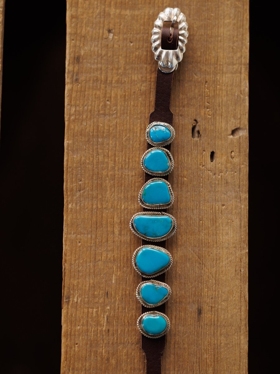 The Aguila Bracelet by Savannah Sevens western life{&}style features six genuine turquoise stones set in sterling silver on leather, displayed on a wooden surface.
