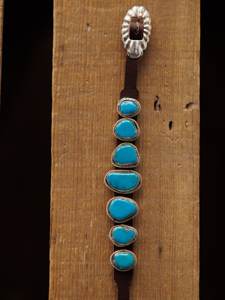 The Aguila Bracelet by Savannah Sevens western life{&}style features six genuine turquoise stones set in sterling silver on leather, displayed on a wooden surface.