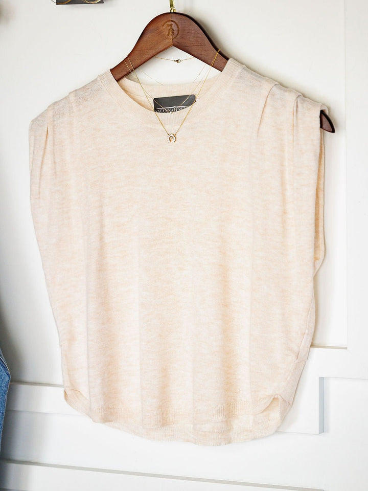 The Alcoa Oatmeal Wool Blend Top by Savannah Sevens western life{&}style, a relaxed-fit, sleeveless top, is displayed on a wooden hanger with a gold necklace over the neck, hanging on a white door.