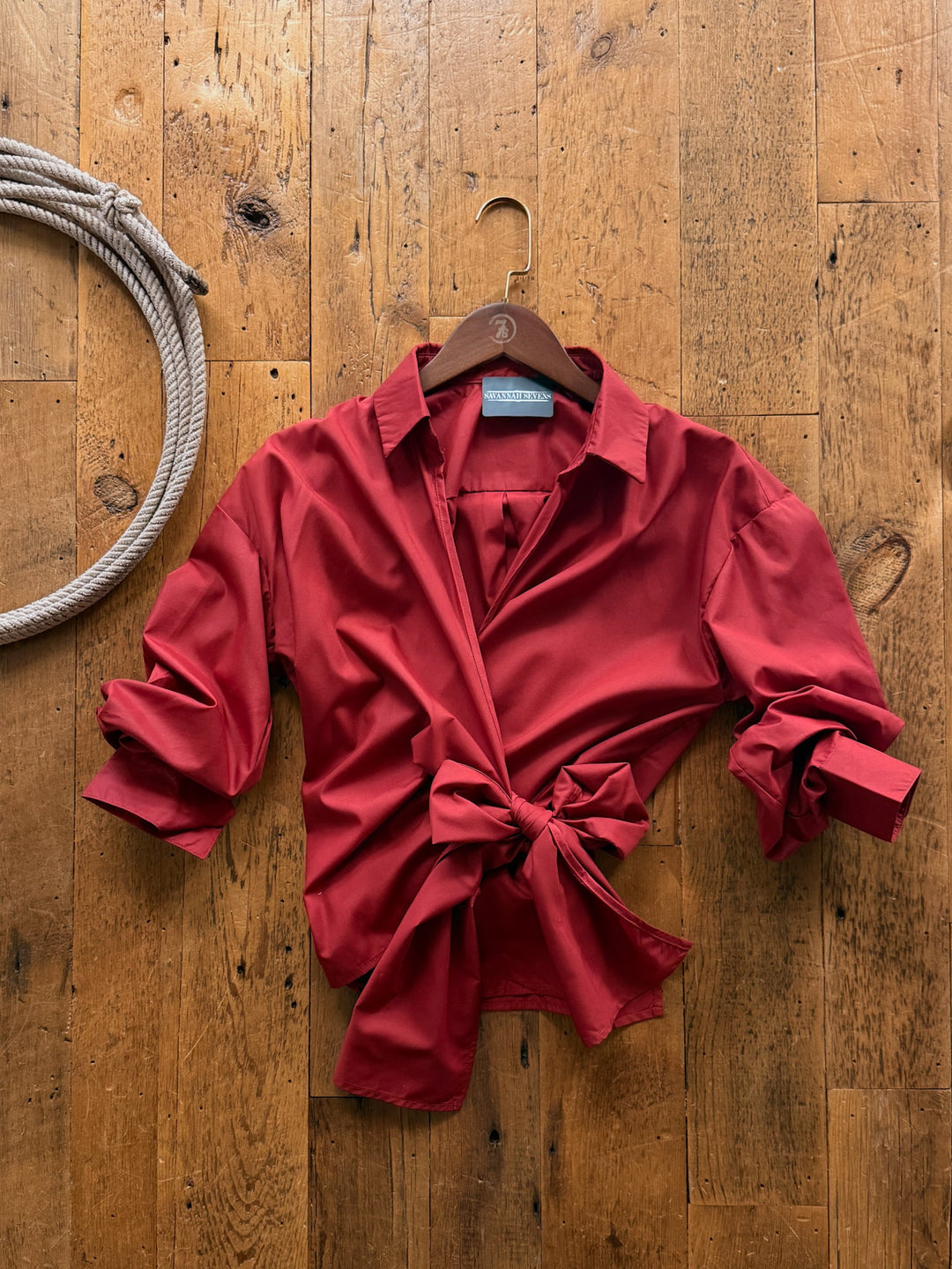 Altamont Red Wrap Top, a red cotton blend 3/4 sleeve wrap top with a front tie, hanging on a wooden hanger against a wooden surface.