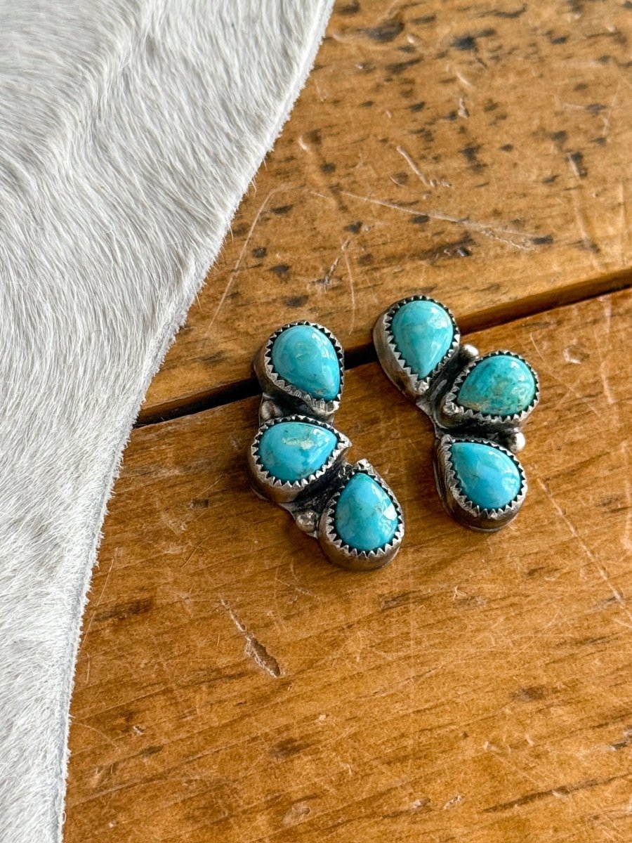 The Amargosa Earrings by Savannah Sevens western life{&}style—sterling silver teardrop earrings with turquoise stones—rest on a wooden surface beside light-colored fur.