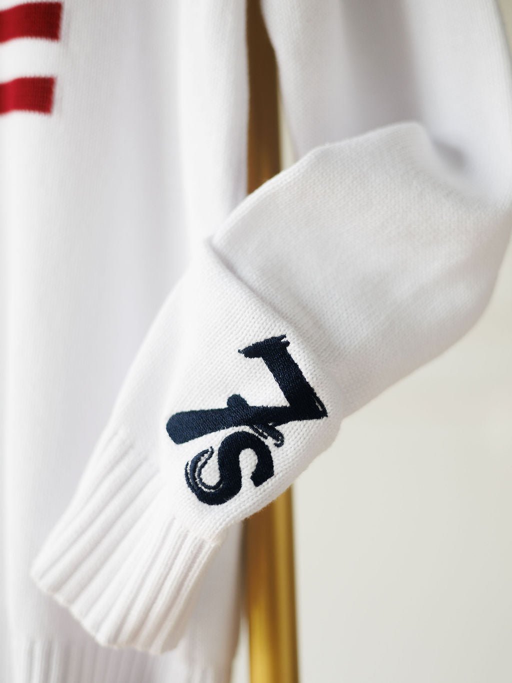 A close-up of The American West {Exclusive} white knit sleeve by Savannah Sevens western life{&}style, featuring a navy 7s logo near the cuff —a signature touch of the brand.