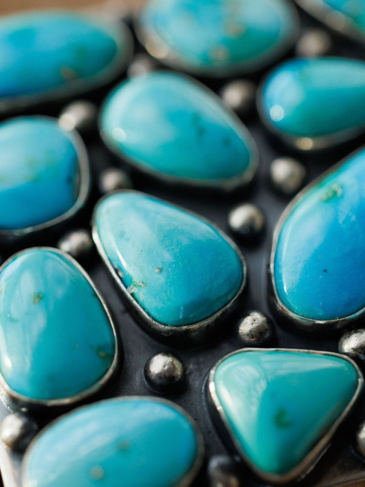 Close-up of polished turquoise stones of various shapes and sizes set in black metal with small silver beads, featuring a glossy finish. Shown: Amorita Buckle by Savannah Sevens western life{&}style.