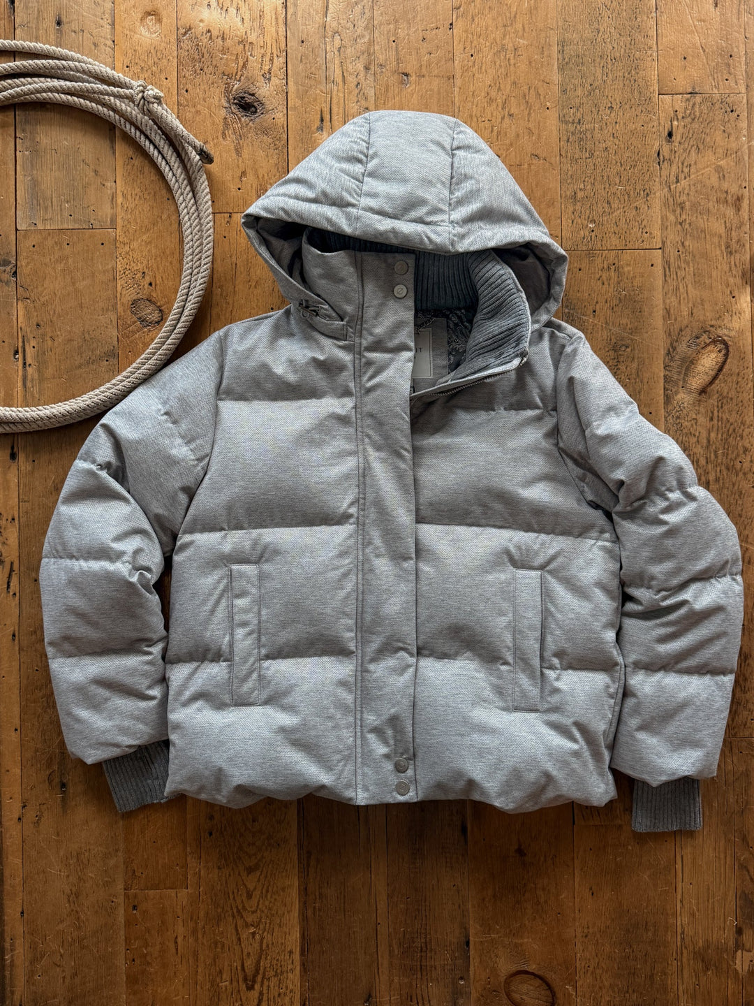 Andover Heather Grey Down Puffer Coat in heather grey with ribbed cuffs, resting on a wooden floor next to a coil of rope.