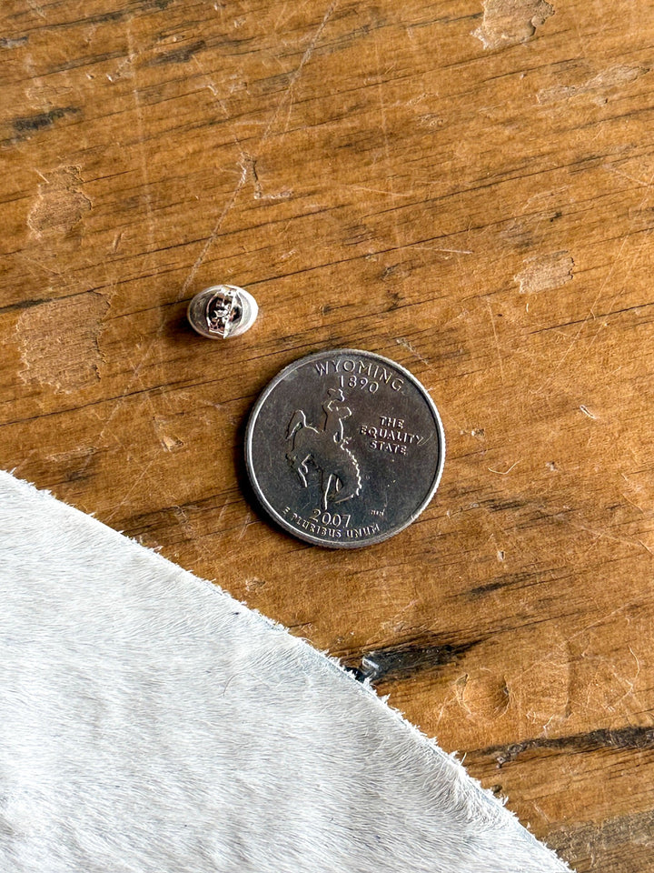 An Anoka Turquoise Stud Earring by Savannah Sevens western life{&}style rests on a wooden surface alongside a 2007 Wyoming state quarter and a small metal earring back, with the corner of light-colored fabric visible—subtly accentuating the striking appeal of these Navajo-inspired studs amid everyday items.