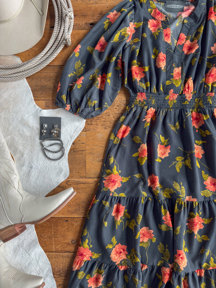Floral print midi dress with red and yellow flowers, featuring a shirred elastic waistline, paired with silver jewelry, white cowboy boots, a white hat, and a coiled rope arranged on a wooden floor.
