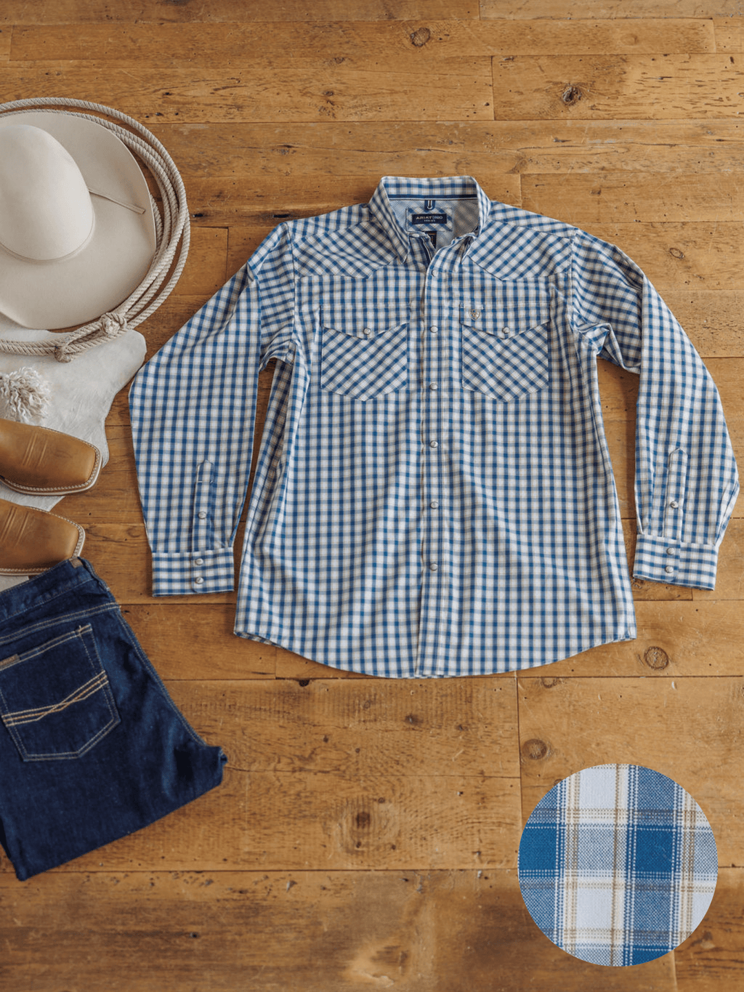 An Ariat Howell Men's Plaid Pearl Snap by Savannah Sevens western life{&}style is laid flat on a wooden floor with a white hat, white boots, blue jeans, and an inset showing the plaid fabric pattern.