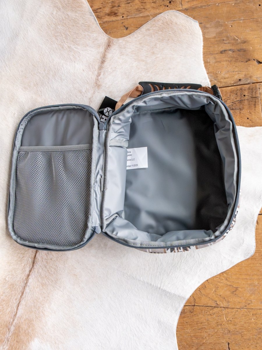 The Arizona Southwest Canvas Lunch Box by Savannah Sevens western life{&}style, open and empty with a waterproof liner and inside mesh pocket, rests on a white cow hide rug atop a wooden floor.