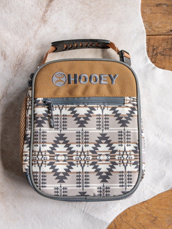 The Arizona Southwest Canvas Lunch Box by Savannah Sevens western life{&}style features a grey, white, and tan southwestern geometric design and waterproof liner, shown on a cowhide rug beside a wooden floor.