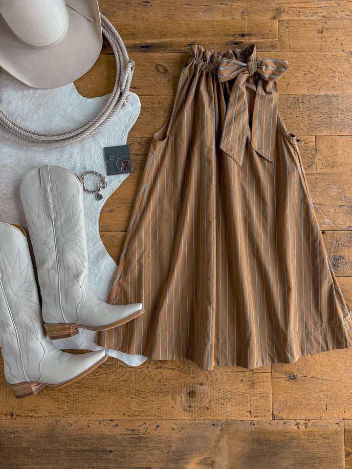 The Ashmore Brown Striped Halter Neck Dress by Savannah Sevens western life{&}style, paired with gray cowboy boots, a gray hat, a cowhide rug, a rope, and earrings, are all arranged on a wooden floor.