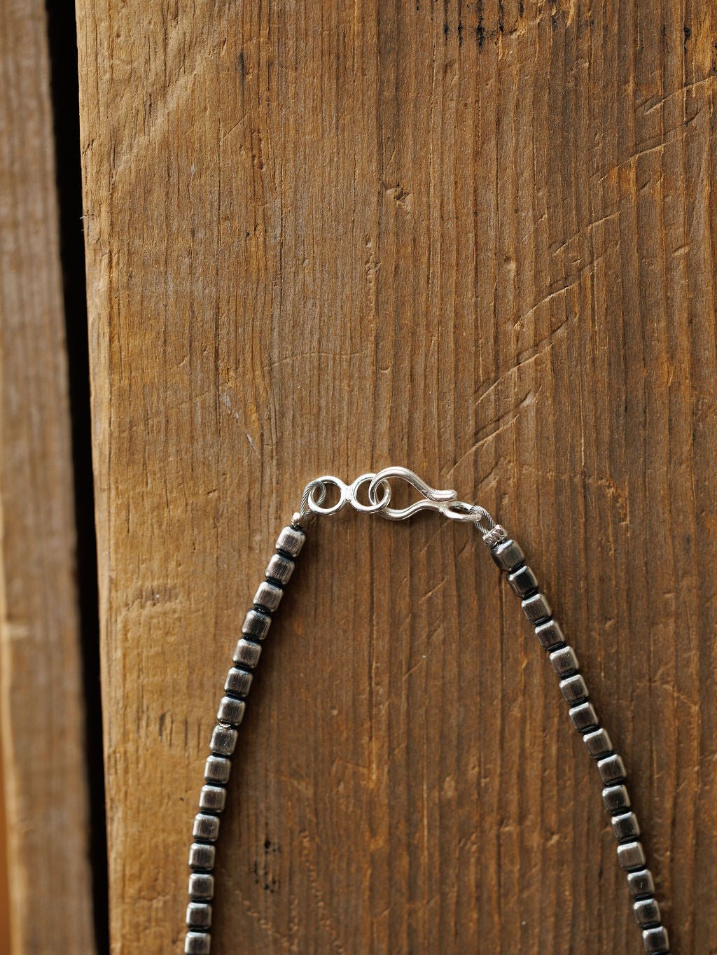 A close-up of the Atoka Necklace by Savannah Sevens western life{&}style, featuring sterling silver square beads and a hook clasp, hanging against a rustic wooden background.
