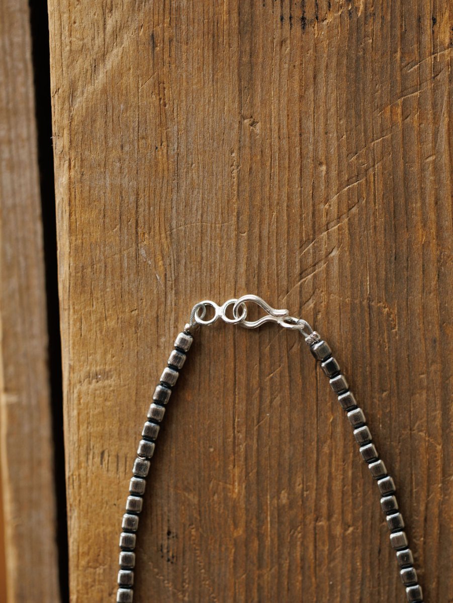 A close-up of the Atoka Necklace by Savannah Sevens western life{&}style, featuring sterling silver square beads and a hook clasp, hanging against a rustic wooden background.