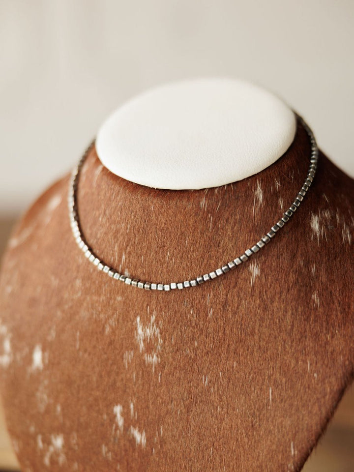 The Atoka Necklace by Savannah Sevens western life{&}style is a thin sterling silver beaded piece inspired by Navajo pearl designs, shown on a brown and white speckled jewelry bust with a white top.